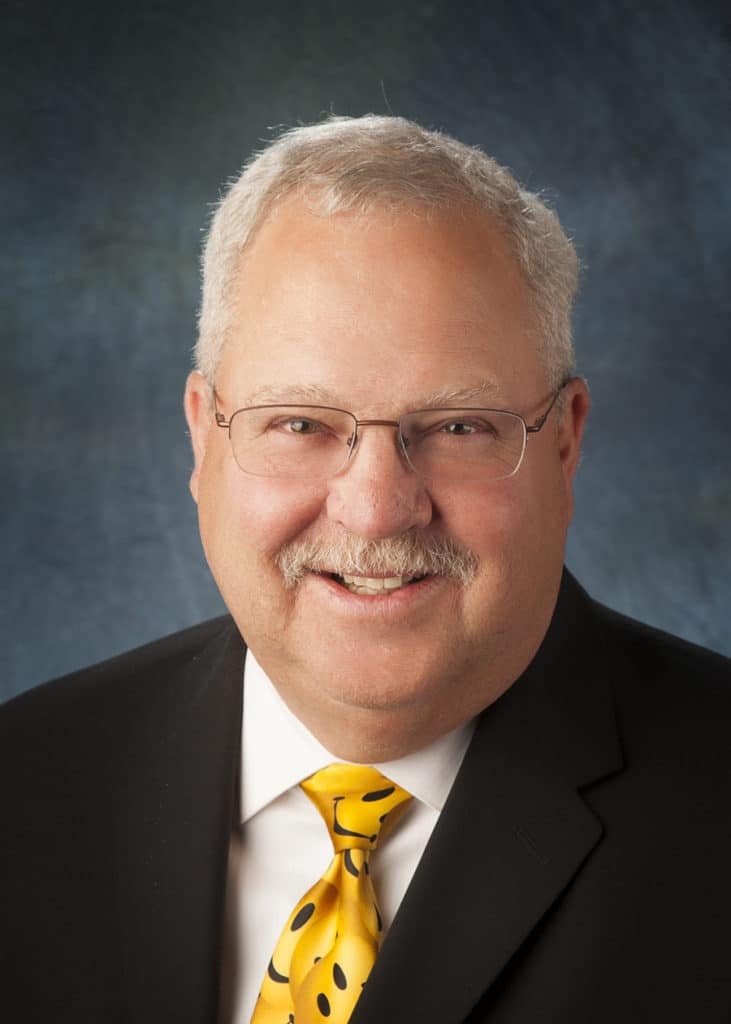 Staff headshot on a blue-gray backdrop for a company website and directory