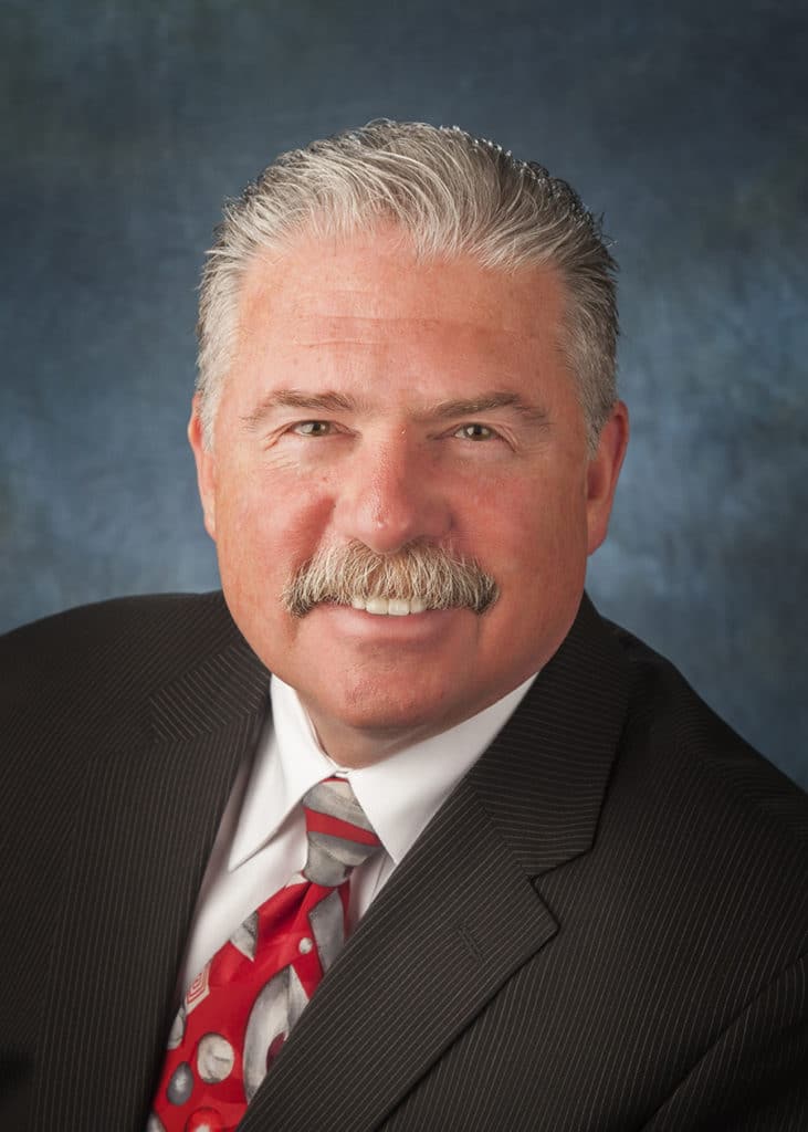 Staff headshot on a blue-gray backdrop for a company website and directory