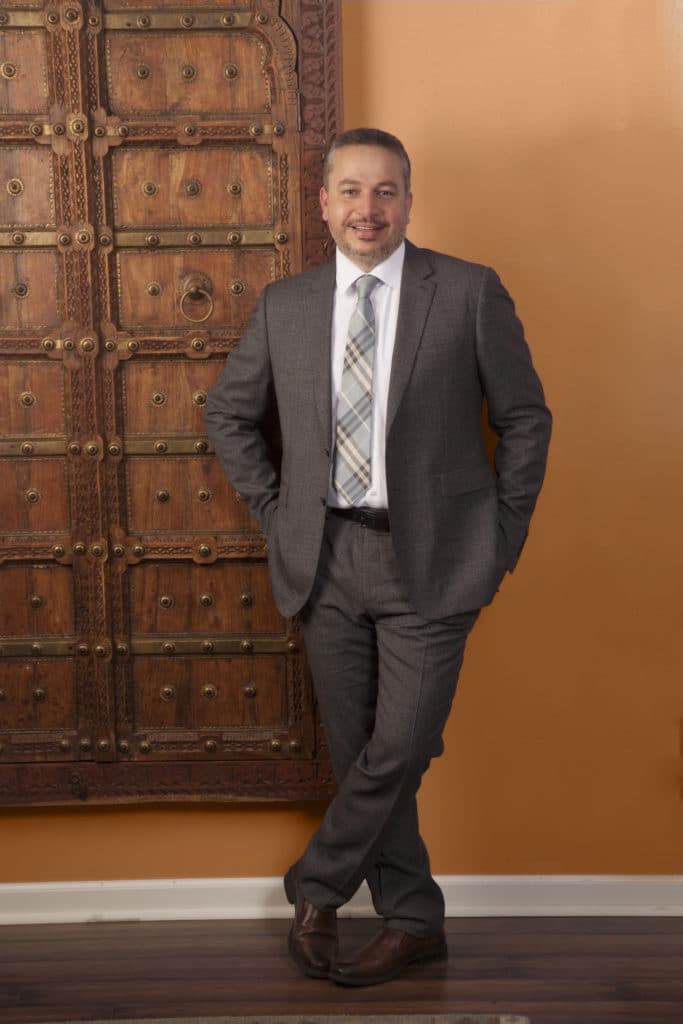 Full-length executive portrait beside a carved wooden door