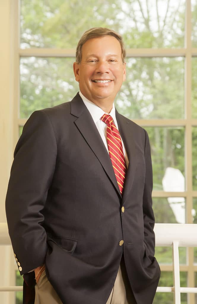 Executive in a dark suit standing by tall office windows