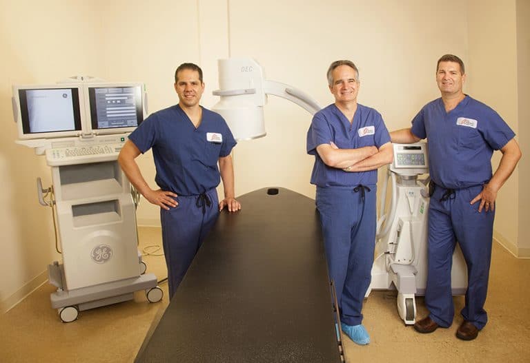 Three surgeons in scrubs beside medical equipment