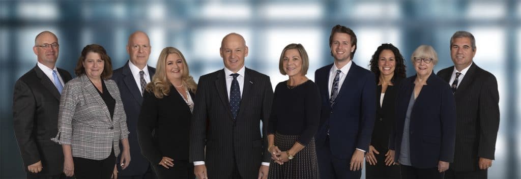Company team photo of fifteen colleagues against an office window backdrop