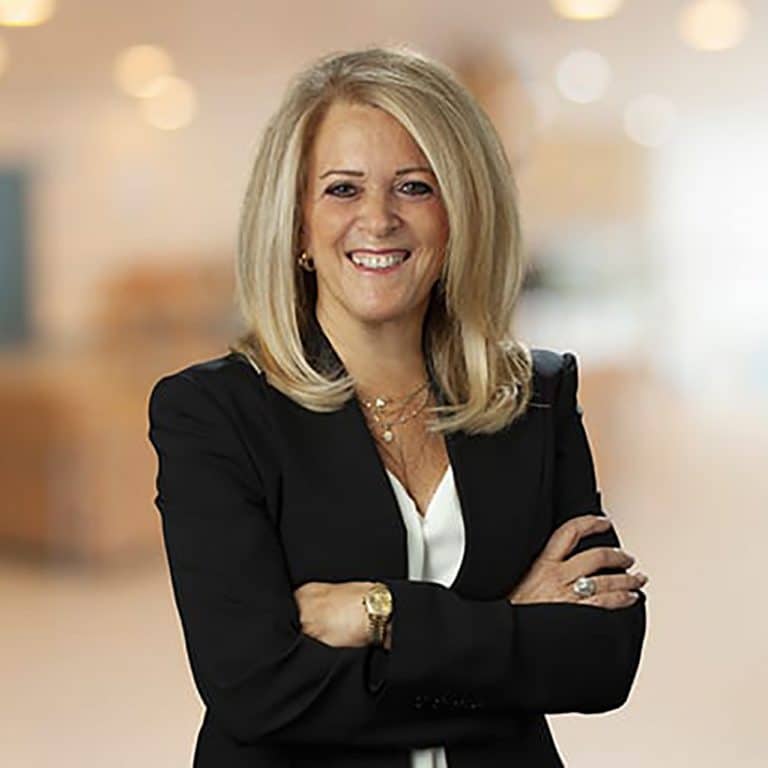Professional woman in a dark blazer with arms crossed, softly blurred office background