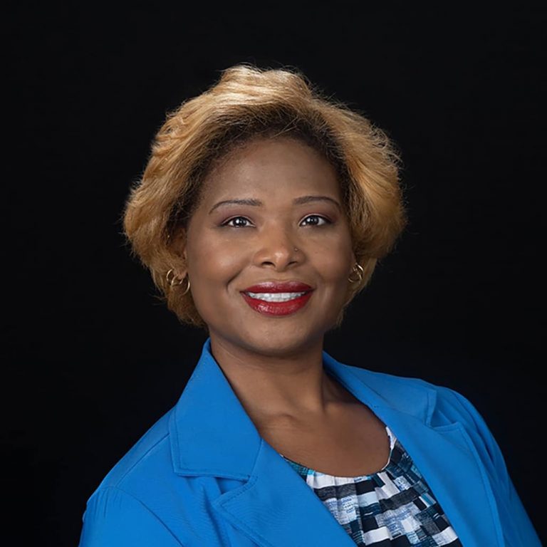 Studio headshot on a black backdrop in a blue blazer